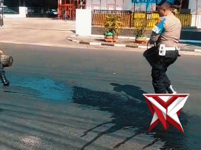 Patroli polsek Kudus membantu membersihkan ceceran tumpahan oli menggunakan air dan serbuk pasir
